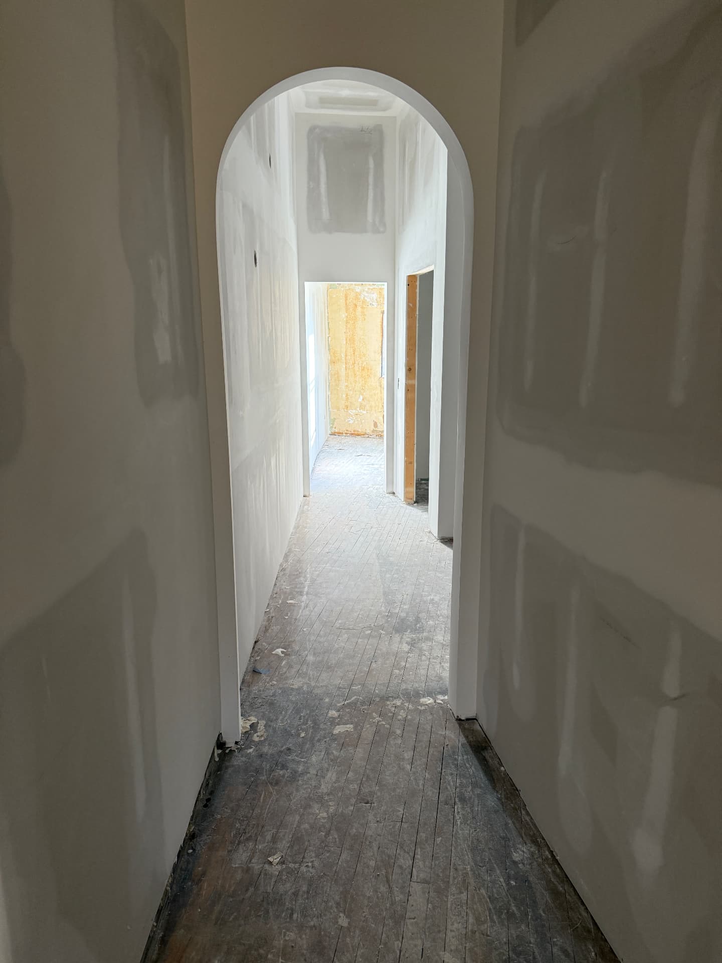 A worn, dusty narrow strip maple hallway under unfinished drywall before sanding
