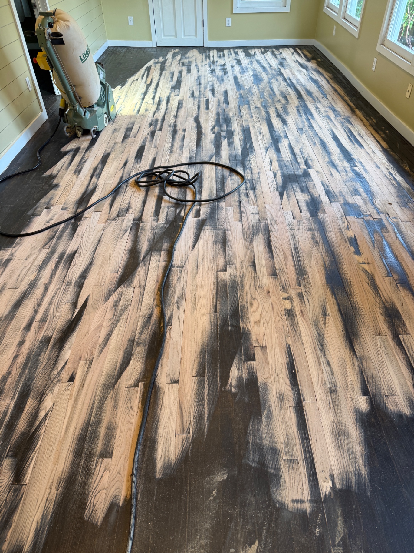 Half-sanded red oak floor in a 1928 craftsman living room during refinishing