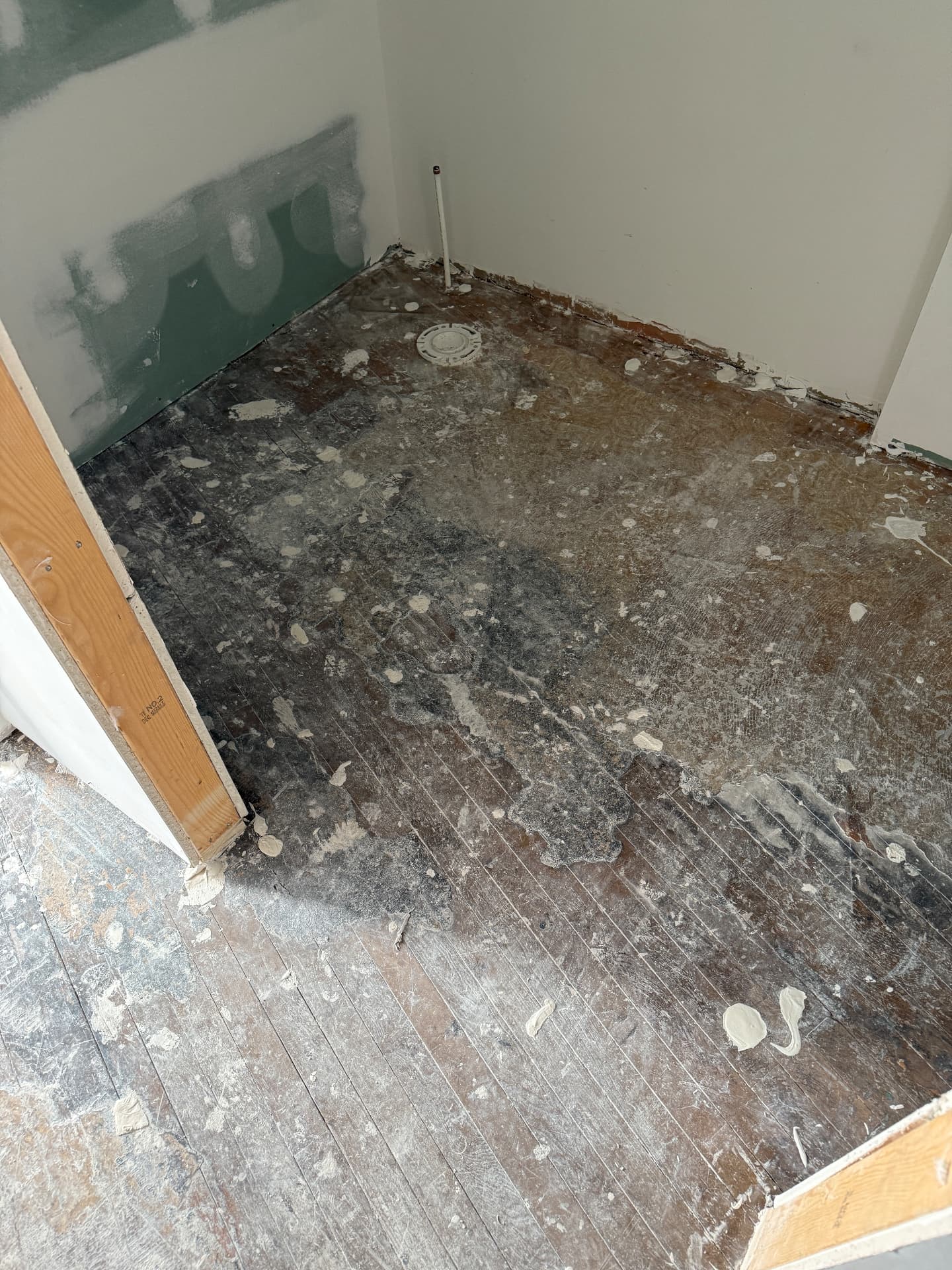 Black mastic adhesive and drywall splatter over narrow strip maple flooring in a small room before sanding