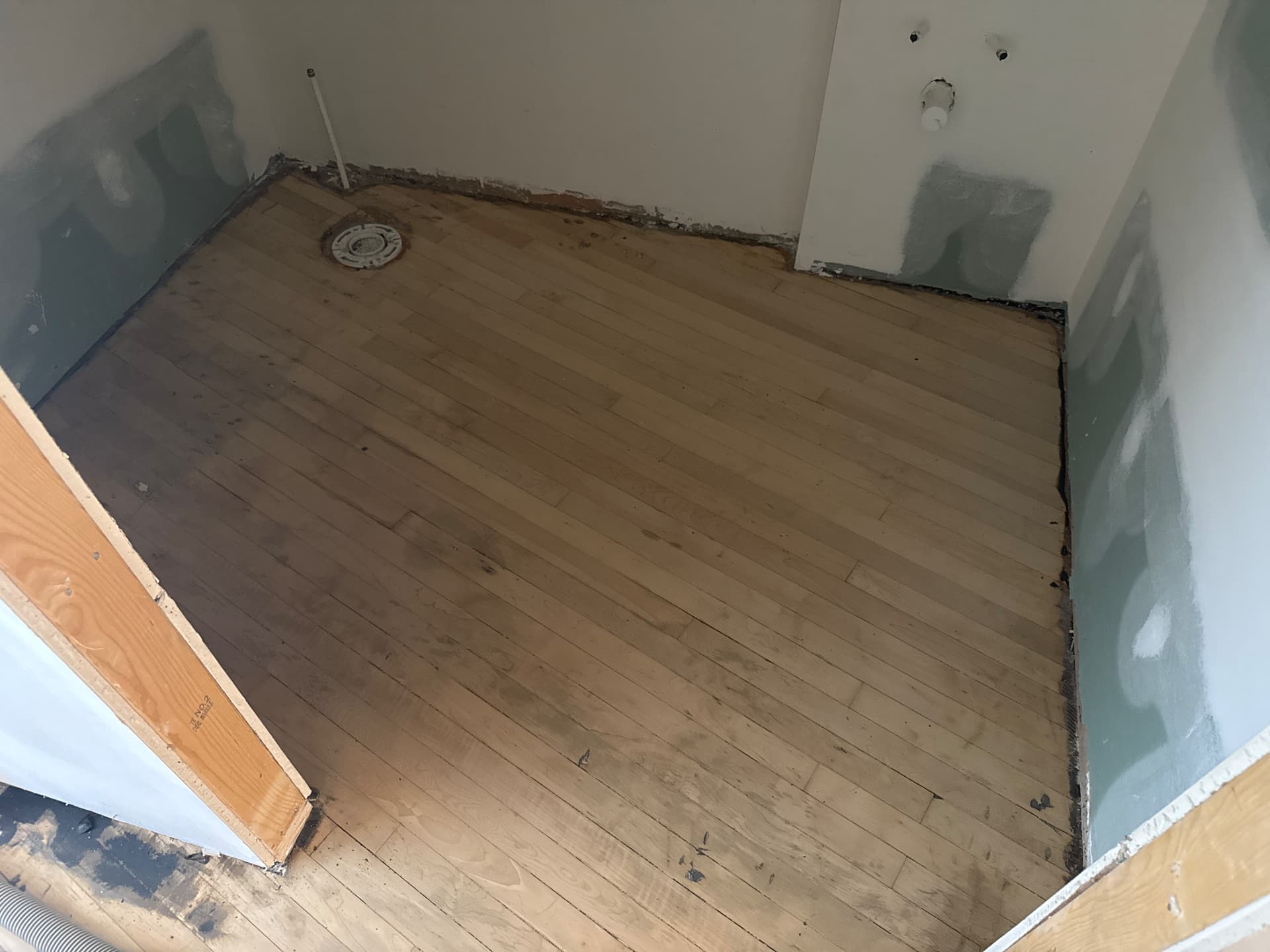 The same small room with the adhesive and splatter sanded off, showing raw bare boards